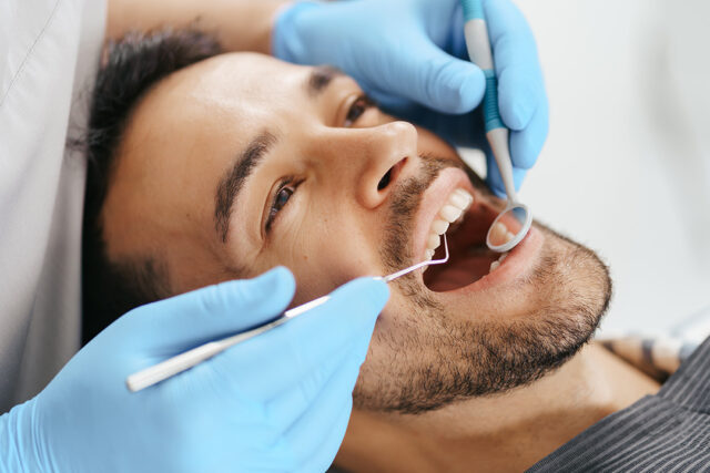smiling young man sitting dentist chair while doctor examining his teeth